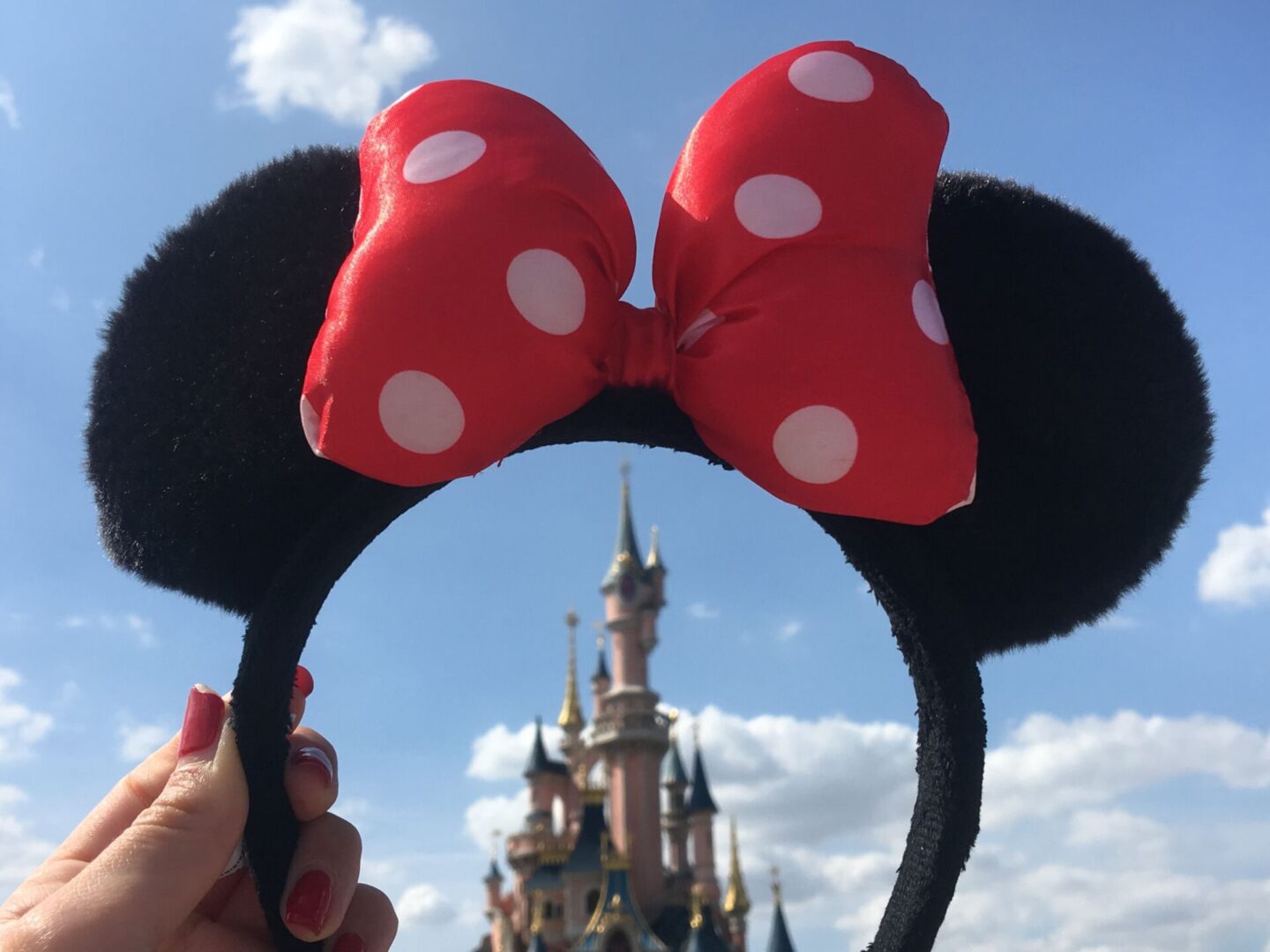 a hand holds up Disney ears in front of a castle at Disneyland